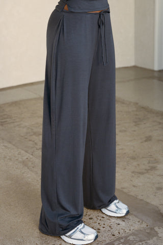 Side view of model from the waist down posing in the relaxed fit navy modal Essential Straight Leg Pant with a wide leg, elastic waistband, adjustable drawstring tie and subtle pleating at the sides.