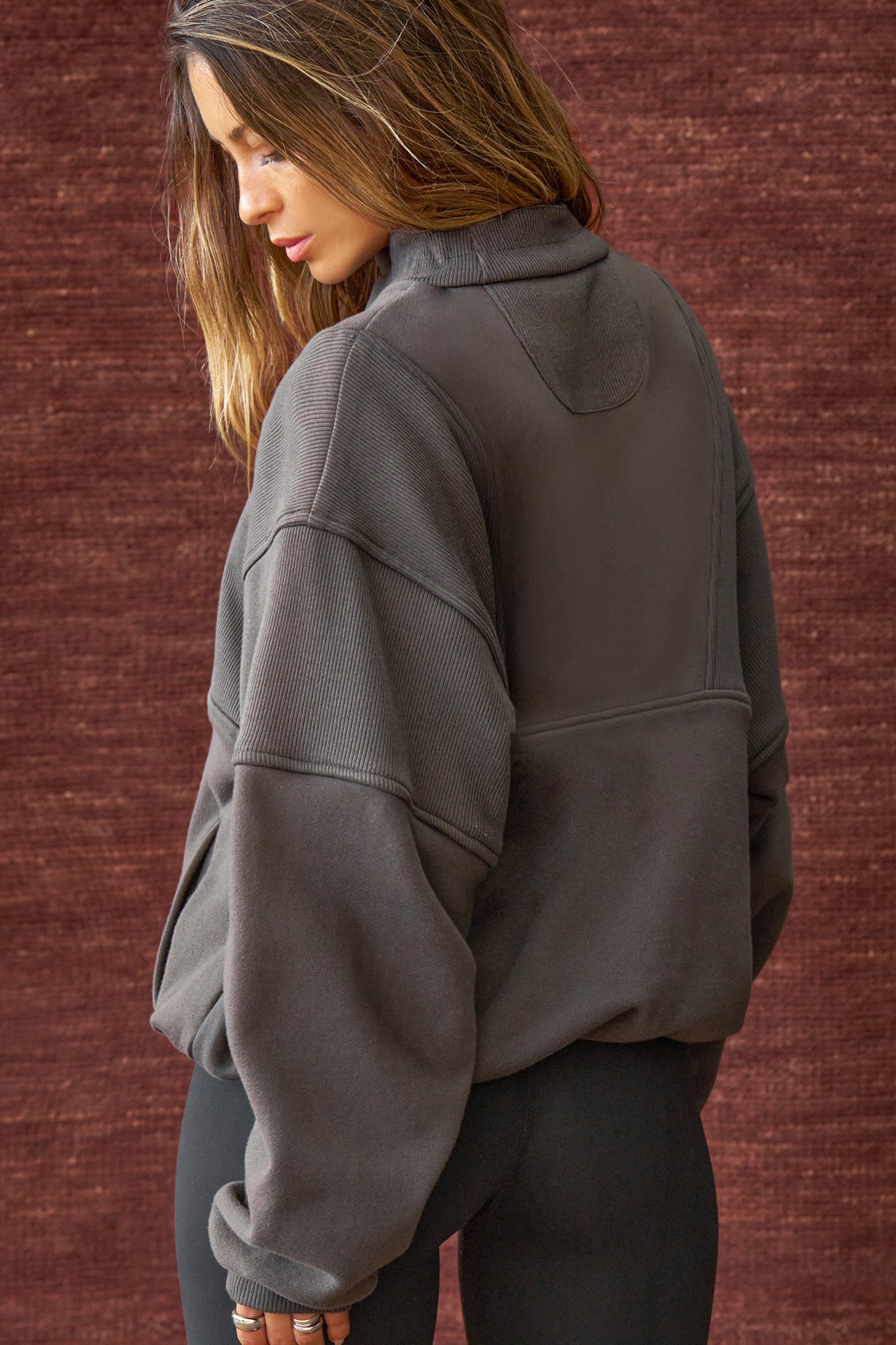 Back view of model posing in the oversized comfortable charcoal luxe french terry Retro Half Zip pullover sweatshirt with ribbed panels and accents on the back and sleeves and a high collar