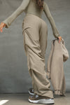 Back view of model posing in the relaxed fit, desert sage nylon Ruched Track Pant with a wide leg, side ruched panels and finished with a drawcord waist, side pockets and adjustable button closures at the ankle.