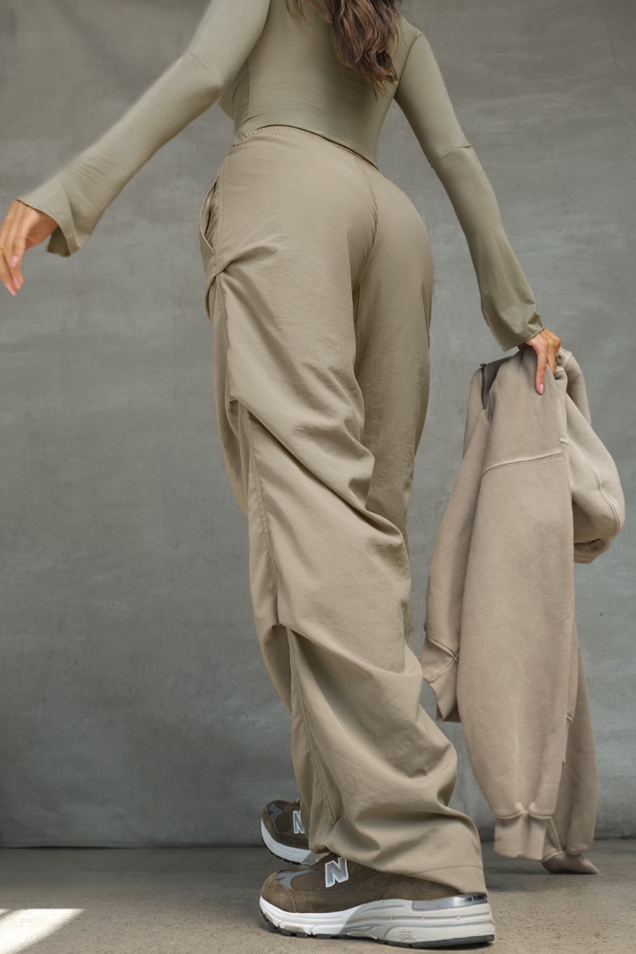 Back view of model posing in the relaxed fit, desert sage nylon Ruched Track Pant with a wide leg, side ruched panels and finished with a drawcord waist, side pockets and adjustable button closures at the ankle.