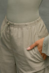 Close up detail side view of model from the waist down posing in the relaxed fit, desert sage nylon Ruched Track Pant with a wide leg, side ruched panels and finished with a drawcord waist, side pockets and adjustable button closures at the ankle.