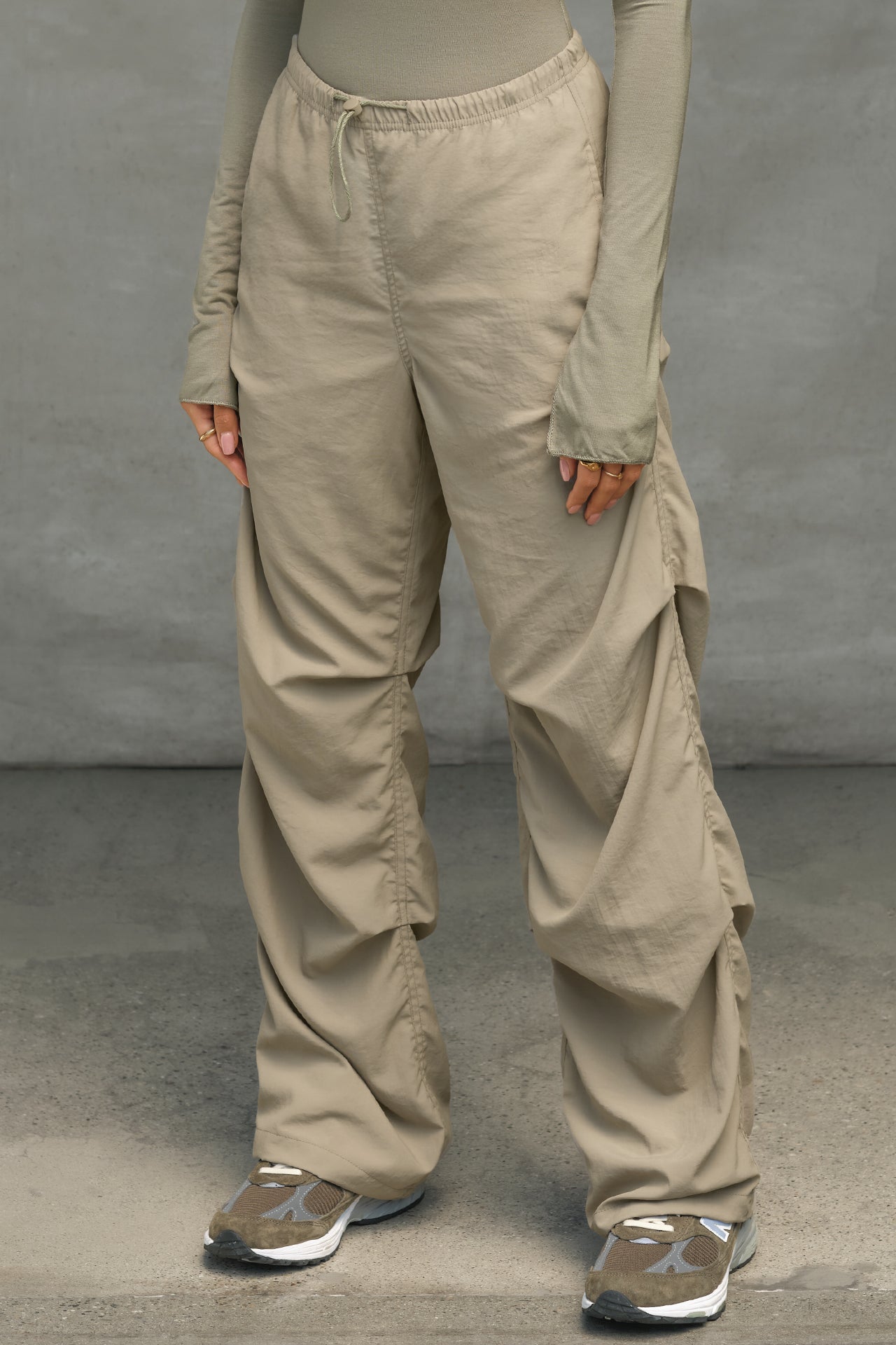 Front view of model from the waist down posing in the relaxed fit, desert sage nylon Ruched Track Pant with a wide leg, side ruched panels and finished with a drawcord waist, side pockets and adjustable button closures at the ankle.
