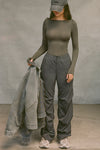 Full body front view of model posing in the relaxed fit, jet nylon Ruched Track Pant with a wide leg, side ruched panels and finished with a drawcord waist, side pockets and adjustable button closures at the ankle.