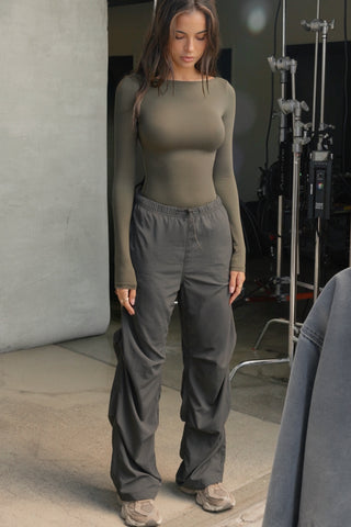 Full body front view of model posing in the relaxed fit, jet nylon Ruched Track Pant with a wide leg, side ruched panels and finished with a drawcord waist, side pockets and adjustable button closures at the ankle.