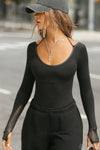 Front view of model posing in the fitted black flexrib Scoop Corset Long Sleeve with a scoop neckline, adjustable ties at the neck, and thumbholes in the mesh sleeves
