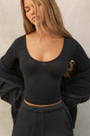 Front view of model posing the fitted lightweight black modal Scoop Neck Long Sleeve top with a deep scoop neckline and fitted sleeves