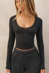 Front view of model posing the fitted lightweight black modal Scoop Neck Long Sleeve top with a deep scoop neckline and fitted sleeves