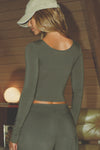 Back view of model posing the fitted lightweight spruce modal Scoop Neck Long Sleeve top with a deep scoop neckline and fitted sleeves