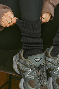 Close up detail front view of model adjusting the slouchy coal Scrunch Sock with extra long ribbed cuffs