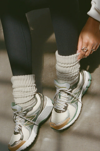 Close up front view of model adjusting the  slouchy off white Scrunch Sock with extra long ribbed cuffs