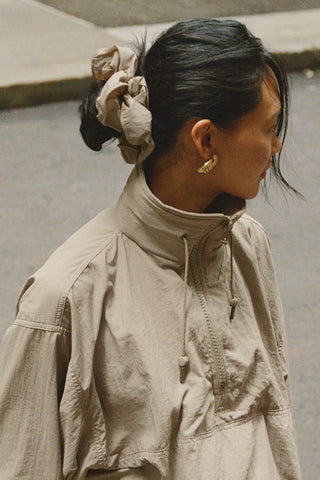 Side view of model posing in the oversized desert sage Nylon Scrunchie with a voluminous silhouette.