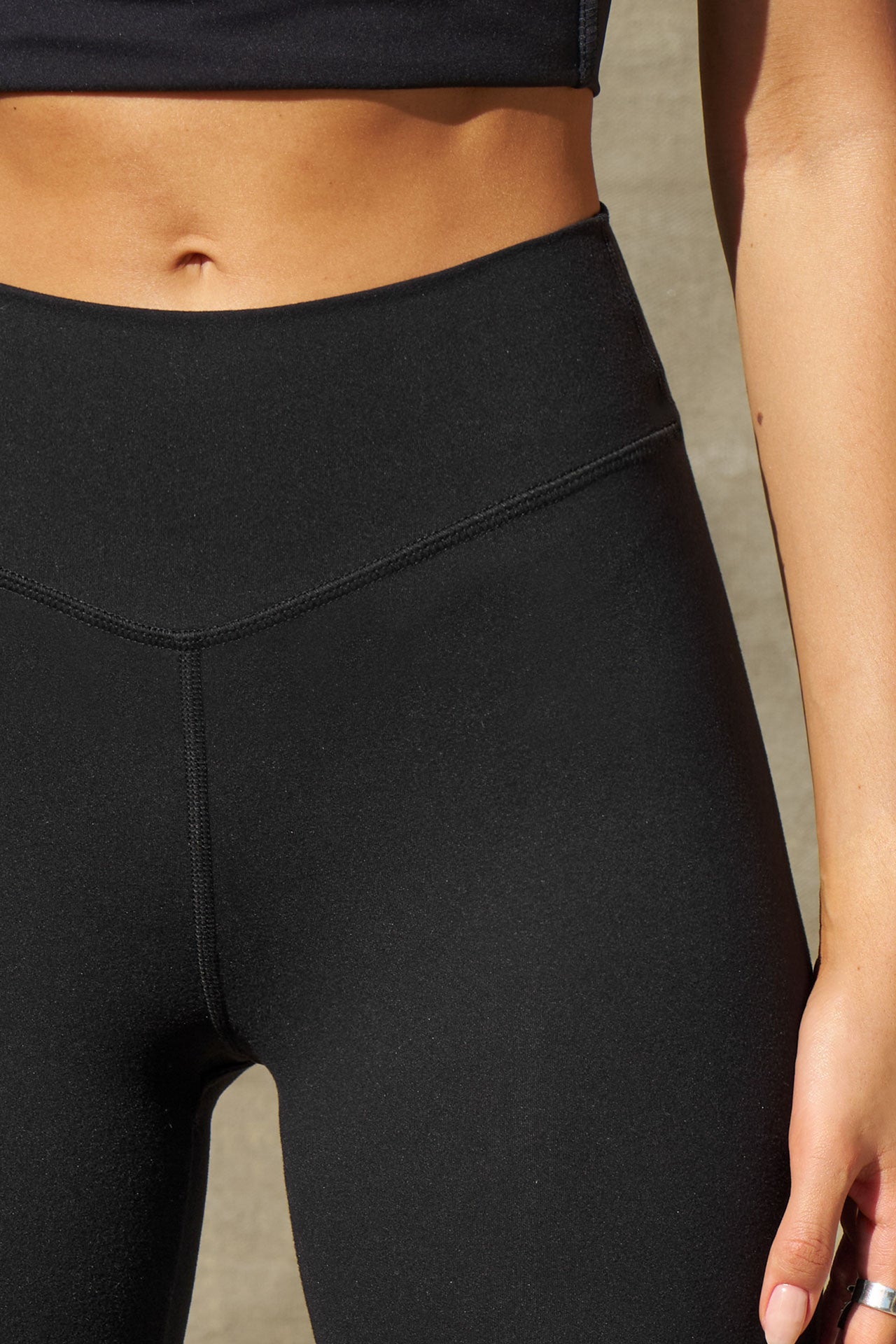 Close up detail front view of model from the waist down posing in the full length bootcut sueded onyx Second Skin Bootcut Legging with a wide v-shaped waistband and split detail at the leg opening