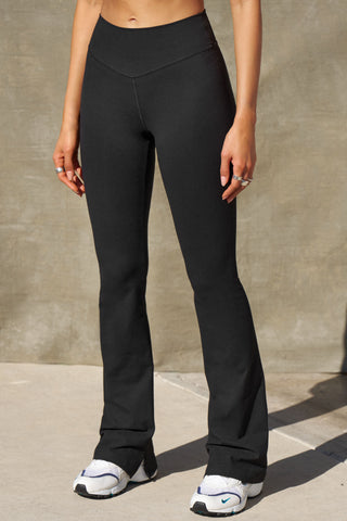 Front view of model from the waist down posing in the full length bootcut sueded onyx Second Skin Bootcut Legging with a wide v-shaped waistband and split detail at the leg opening