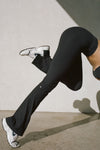 Side view of model from the waist down posing in the full length bootcut sueded onyx Second Skin Bootcut Legging with a wide v-shaped waistband and split detail at the leg opening