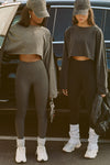 Two models posing in front of a car wearing the haze cotton and washed black cotton Slouchy Crop Long Sleeve and the sueded carob and sueded onyx Second Skin Legging
