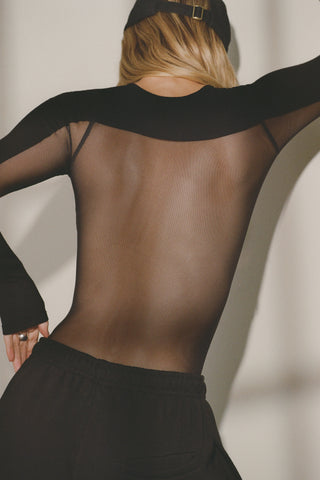 Back view of model posing in fitted black flexrib Sheer Back Long Sleeve top with a crew neckline and sheer mesh back panel.