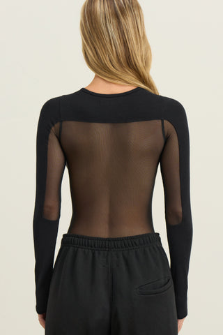 Back view of model posing in fitted black flexrib Sheer Back Long Sleeve top with a crew neckline and sheer mesh back panel.