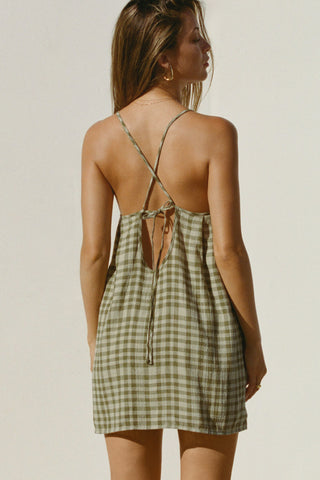 Back view of model posing in the lightweight orchard gauze Shift Mini Dress with a scoop neckline, front keyhole detail and open back with adjustable straps and a tie closure