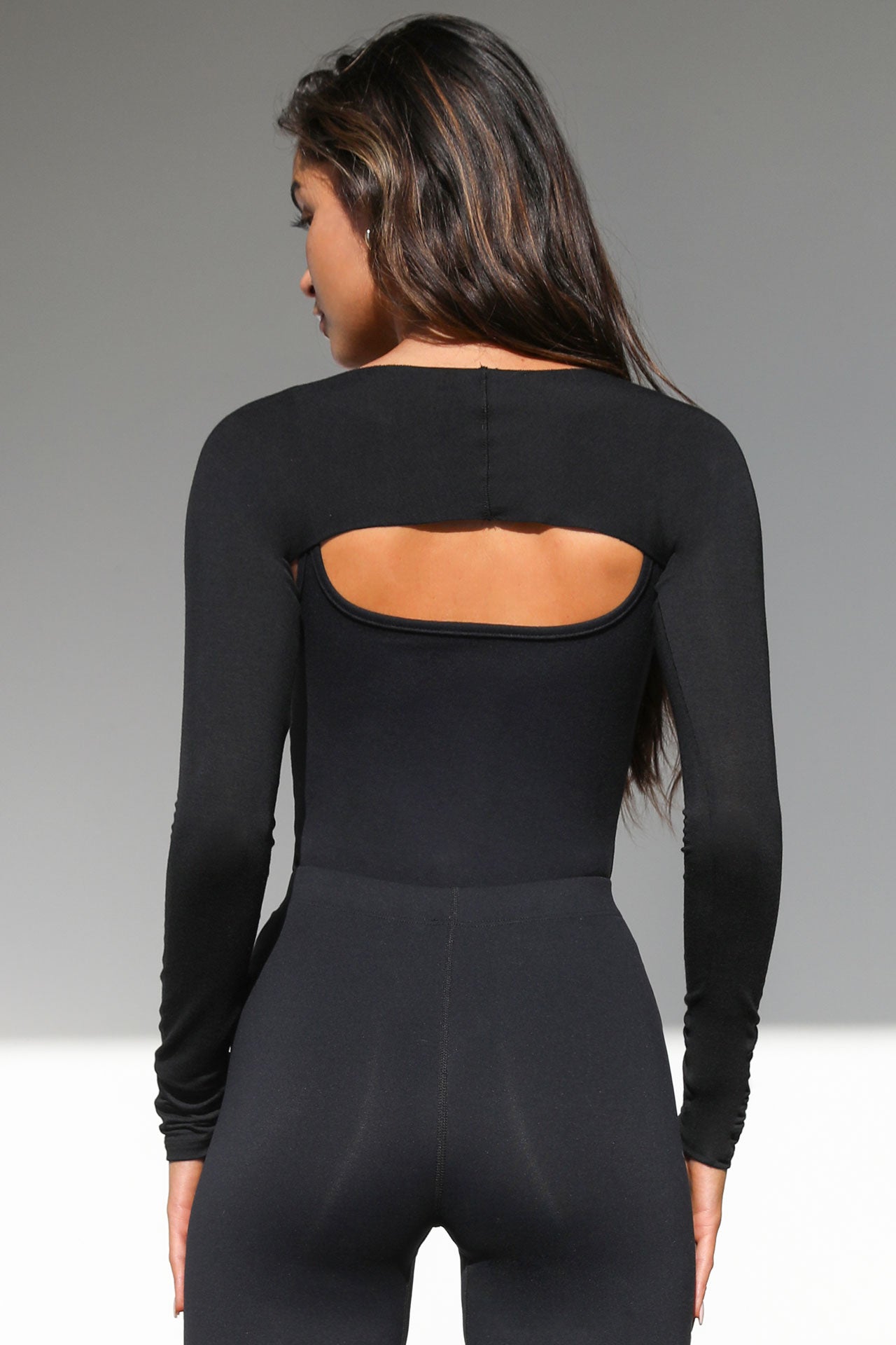 Back view of model posing in the ultra cropped black modal Shrug cardigan with fitted long sleeves