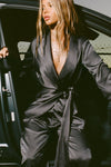 Front view of model getting out of a car in the smooth and soft iron Silk Wrap Blazer top with an adjustable tie waist and shawl collar neckline.
