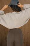 Back view of model posing in the cropped relaxed fit sandstone cotton Slouchy Crop Long Sleeve top with a crew neckline, dropped shoulders and oversized sleeves