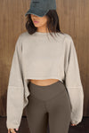 Front view of model posing in the cropped relaxed fit sandstone cotton Slouchy Crop Long Sleeve top with a crew neckline, dropped shoulders and oversized sleeves