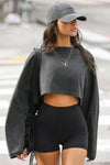 Front view of model posing in the cropped relaxed fit washed black cotton slouchy crop long sleeve top with a crew neckline, dropped shoulders and oversized sleeves