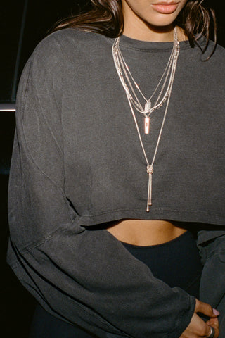 Close up detail front view of model posing in the cropped relaxed fit washed black cotton Slouchy Crop Long Sleeve top with a crew neckline, dropped shoulders and oversized sleeves