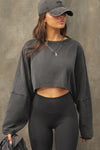 Front view of model posing in the cropped relaxed fit washed black cotton Slouchy Crop Long Sleeve top with a crew neckline, dropped shoulders and oversized sleeves