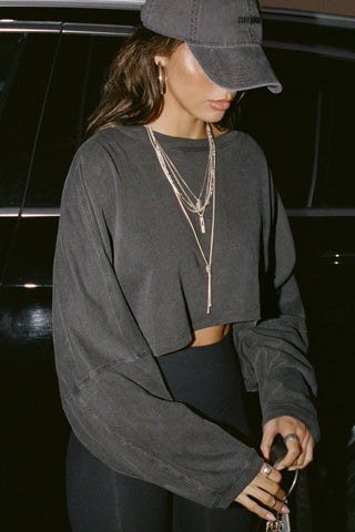 Side view of model posing in the cropped relaxed fit washed black cotton Slouchy Crop Long Sleeve top with a crew neckline, dropped shoulders and oversized sleeves