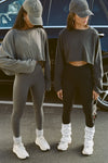 Two modelsl posing in the cropped relaxed fit washed black cotton Slouchy Crop Long Sleeve top and the haze cotton Slouchy Crop Long Sleeve top with a crew neckline, dropped shoulders and oversized sleeves