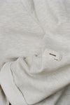 Close up detail view of the oversized pearl grey french terry Slouchy Pullover Sweatshirt with a wide, off-the-shoulder neckline and a JOAH BROWN logo patch on the right sleeve