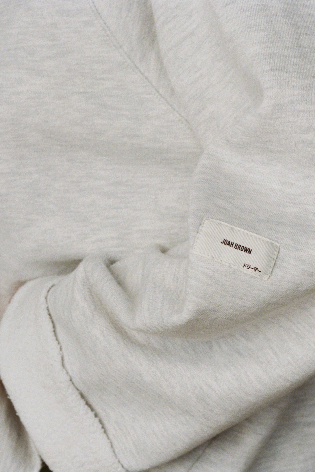 Close up detail view of the oversized pearl grey french terry Slouchy Pullover Sweatshirt with a wide, off-the-shoulder neckline and a JOAH BROWN logo patch on the right sleeve