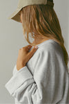 Close up side view of model posing in the oversized pearl grey french terry Slouchy Pullover Sweatshirt with a wide, off-the-shoulder neckline and a JOAH BROWN logo patch on the right sleeve