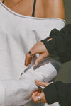 Close up detail front view of model posing in the oversized pearl grey french terry Slouchy Pullover Sweatshirt with a wide, off-the-shoulder neckline and a JOAH BROWN logo patch on the right sleeve