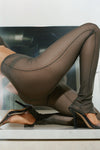 Close up side view of model from the waist down posing in the sheer high-waisted graphite mesh Split Hem Legging with gathered ankles, exposed seams and button closures at the leg opening
