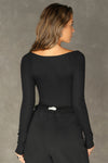 Back view of model posing in the fitted and stretchy black rib Square Neck Long Sleeve top with a wide square neckline