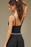 Back view of model posing in the fitted and slightly cropped black flexrib Strappy Scoop Tank with a scoop neckline and adjustable straps. 