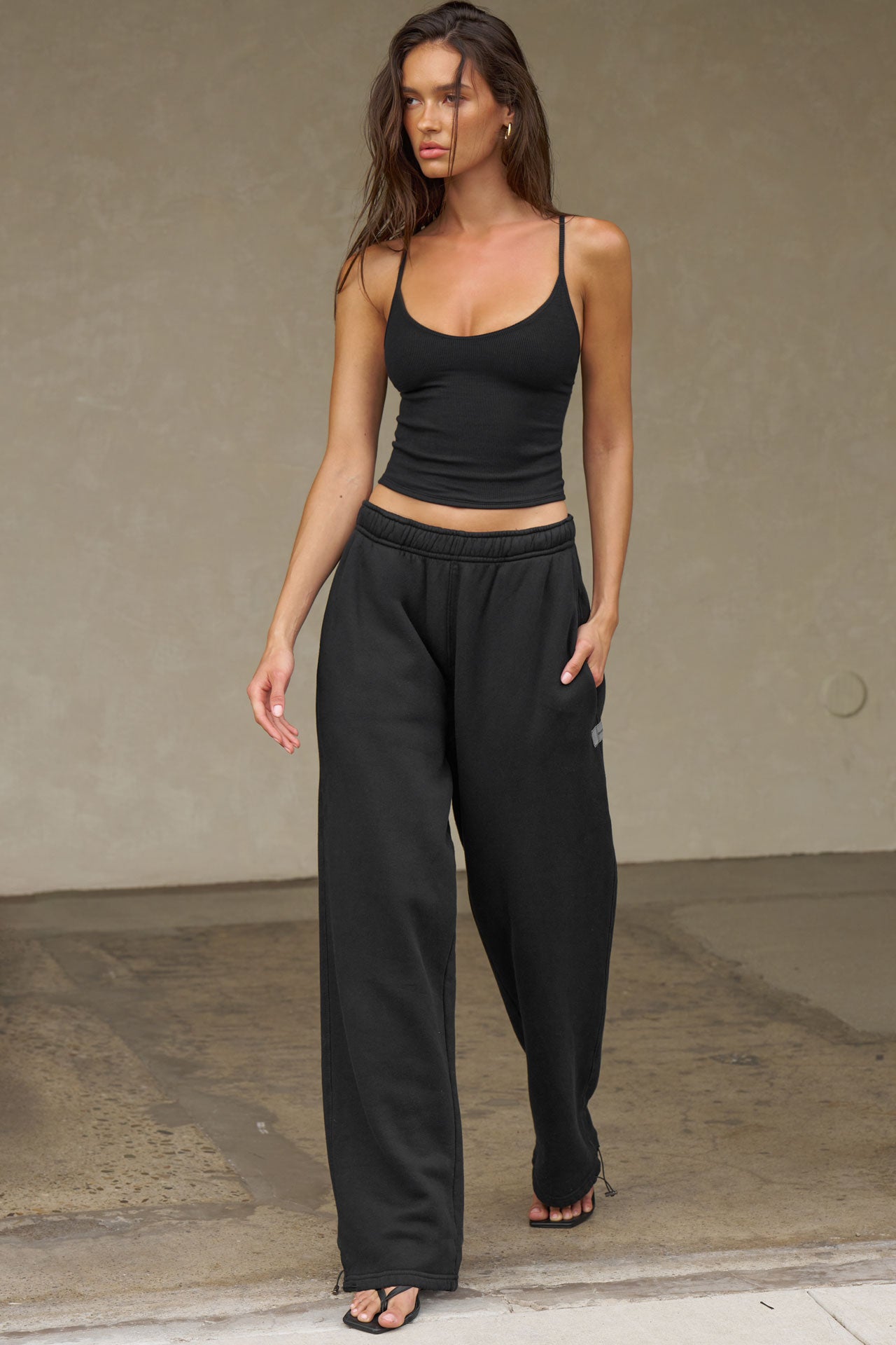 Full body front view of model posing in the fitted and slightly cropped black flexrib Strappy Scoop Tank with a scoop neckline and adjustable straps. 
