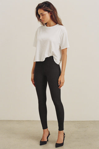Full body front view of model posing in the sleek and stretchy full length sueded onyx The Body Legging with a mid-rise elastic waistband