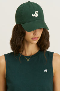 Front view of model posing in the structured six-panel  alpine The Classic Cap with a curved brim, adjustable back strap and an embroidered front and back Joah Brown logo
