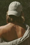 Back view of model posing outside wearing the six-panel sahara Official Cap with a curved brim and an embroidered upside down Joah Brown logo on the front