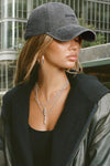 Side view of model posing outside in the six-panel washed black Official Cap with a curved brim and an embroidered upside down Joah Brown logo on the front