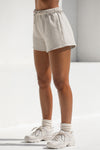 Side view of model from the waist down posing in the relaxed fit sahara french terry Sweat Short with side pockets, hidden drawstring, and an adjustable elastic waistband.