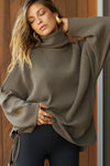 Front view of model posing in the relaxed and slouchy tunic-style army luxe knit Turtleneck Tunic with dropped shoulders, side slits and adjustable ties for a customized shape