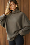 Front view of model posing in the relaxed and slouchy tunic-style army luxe knit Turtleneck Tunic with dropped shoulders, side slits and adjustable ties for a customized shape