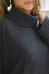Close up detail front view of model posing in the relaxed and slouchy tunic-style midnight luxe knit Turtleneck Tunic with dropped shoulders, side slits and adjustable ties for a customized shape