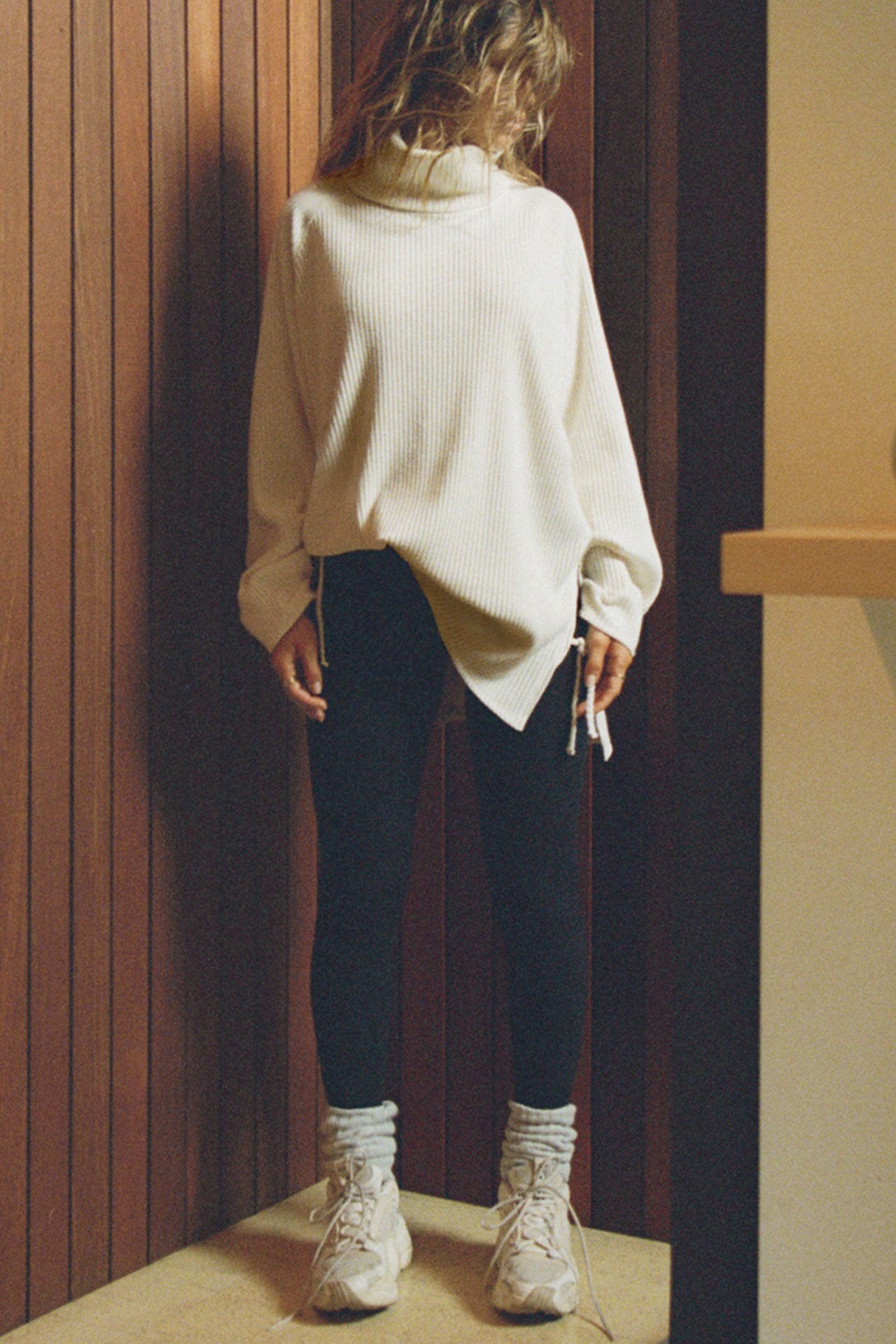 Full body front view of model posing in the relaxed and slouchy tunic-style natural luxe knit Turtleneck Tunic with dropped shoulders, side slits and adjustable ties for a customized shape