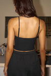 Back view of model posing in the fitted and slightly cropped black flexrib Strappy Scoop Tank with a scoop neckline and adjustable straps. 