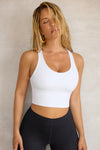 Front view of model posing in the fitted stretchy cropped white flexrib Varsity Tank Bra with a scoop neckline